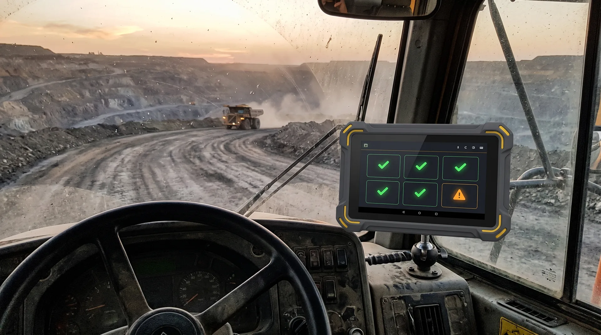 Inside the cab of a rock truck at dusk: the Firefly hub, a rugged touchscreen with yellow corner bumpers on a ball mount beside the wheel, showing five green checks and one amber warning, with the haul road ahead.